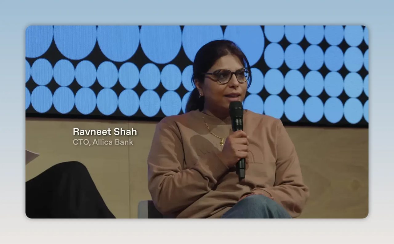 Ravneet Shah นั่งถือไมโครโฟนบนเวที พร้อมข้อความชื่อและตำแหน่ง CTO Allica Bank